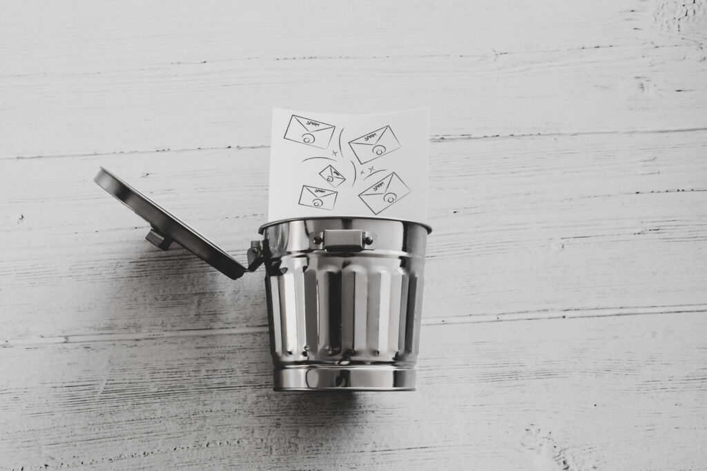 Concept art of a metal trash can and drawn spam email envelopes entering it indicating it's better to delete spam instead of blocking.