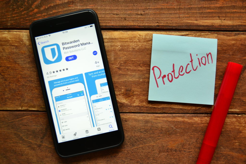 Smartphone with download page for Bitwarden next to Post-It with "Protection" written in red marker.