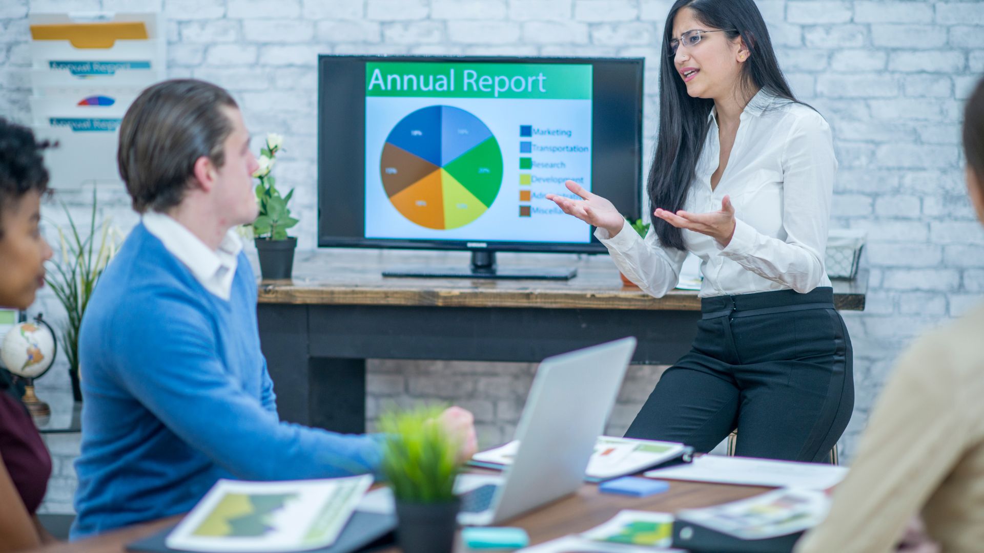 Woman presenting data in a meeting. A man whose laptop is hacked, has his laptop's speaker listening and recording the meeting