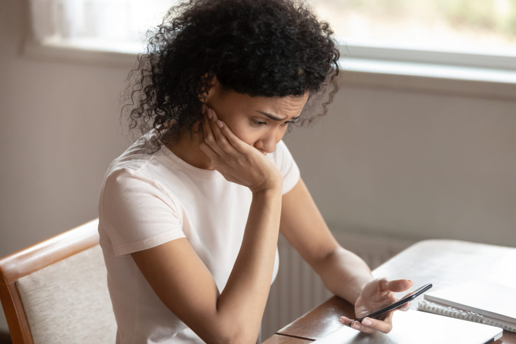 Worried woman at her desk holding her smartphone wondering "Can texts be traced"