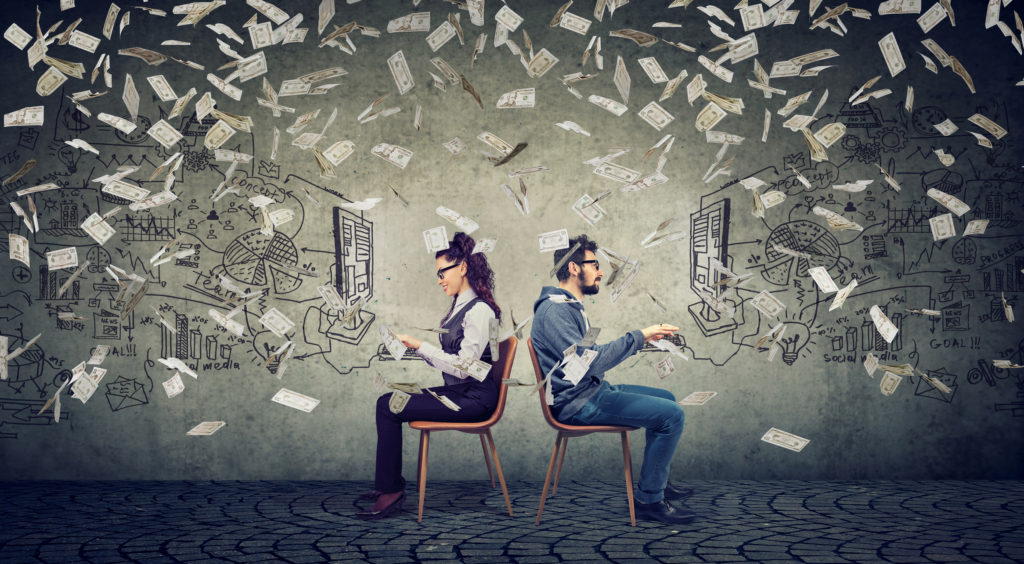 A female and male tech professional sit at computers with money raining down around them.