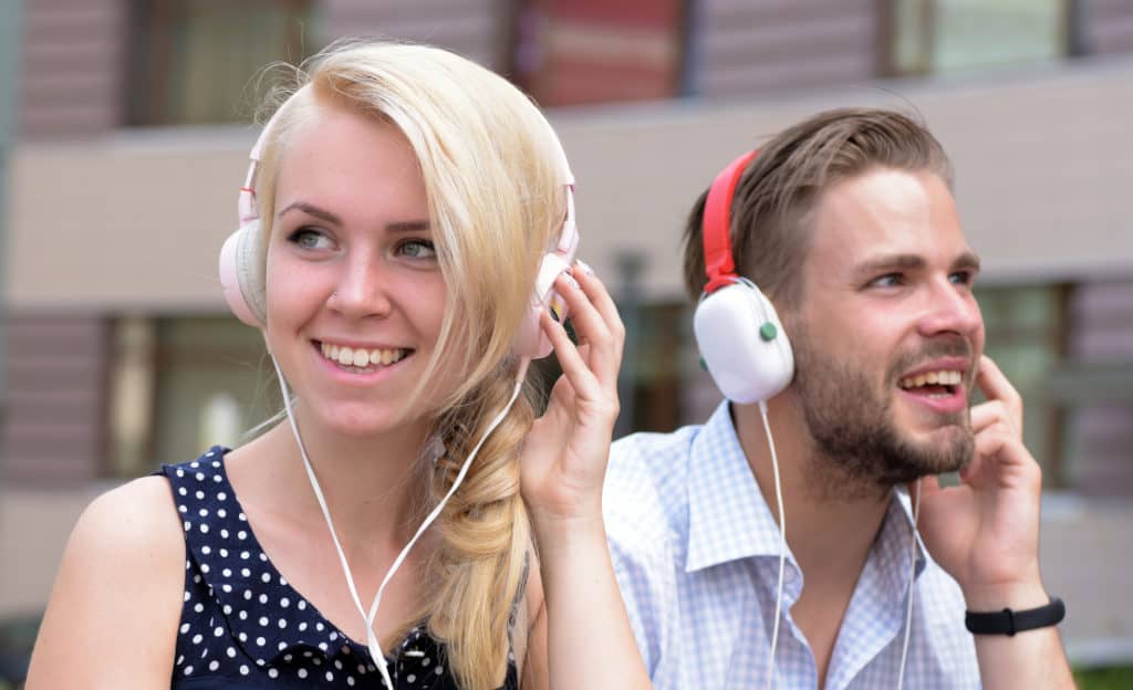 A couple wearing wired headphones instead of a Bluetooth hub to connect multiple Bluetooth headphones.