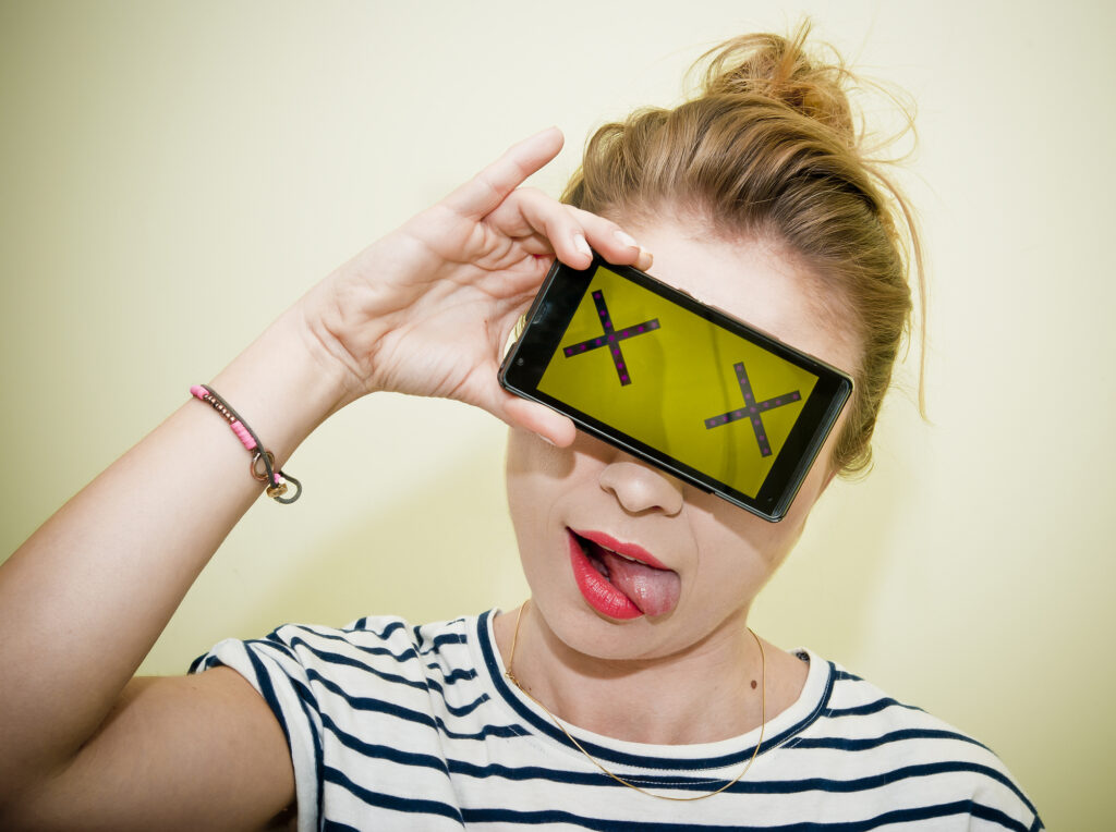 Photo of a teen holding a smartphone in front of her eyes signaling a dead battery.