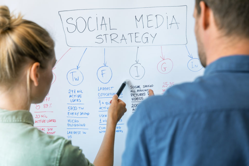 Female and male Social Media managers standing in front of a whiteboard working on their social media strategy.