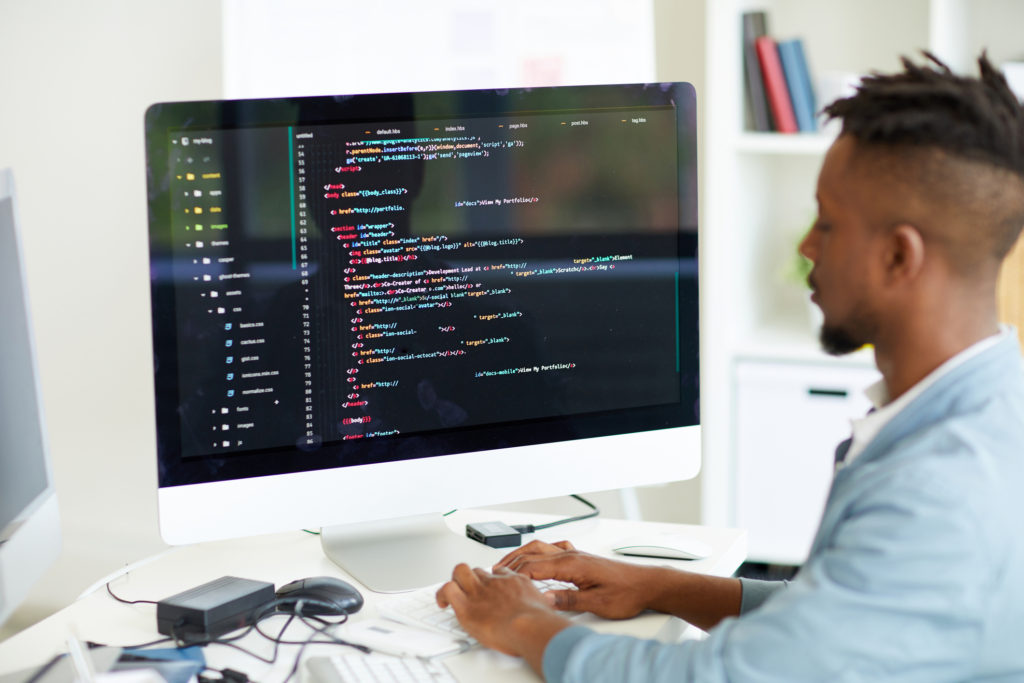 A male Web Developer at his desk with a large computer screen full of code.