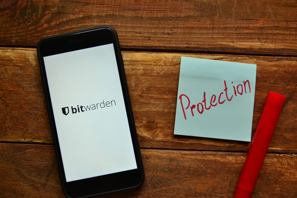 Smartphone with Bitwarden start screen next to a sticky note with the word "protection"