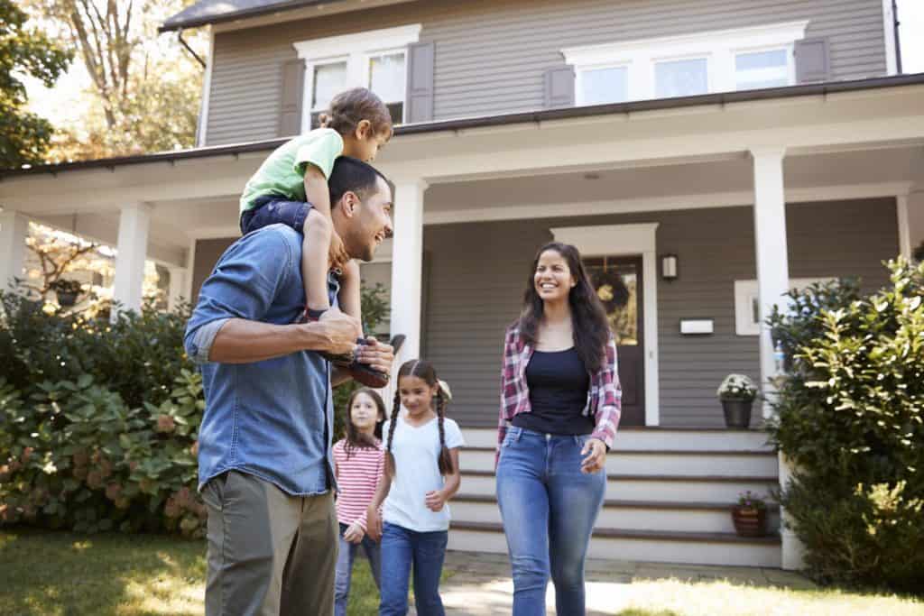 Smiling woman and her family outside their nice home that she worked hard in her cyber security job