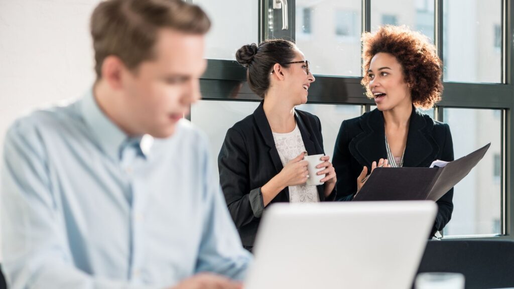 an introvert male working on his laptop, two extrovert females laughing and discussing, all of them are computer engineers