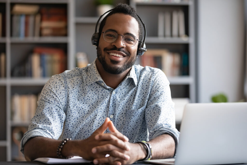 Man working at Help Desk wearing a headset in front of a laptop and smiling