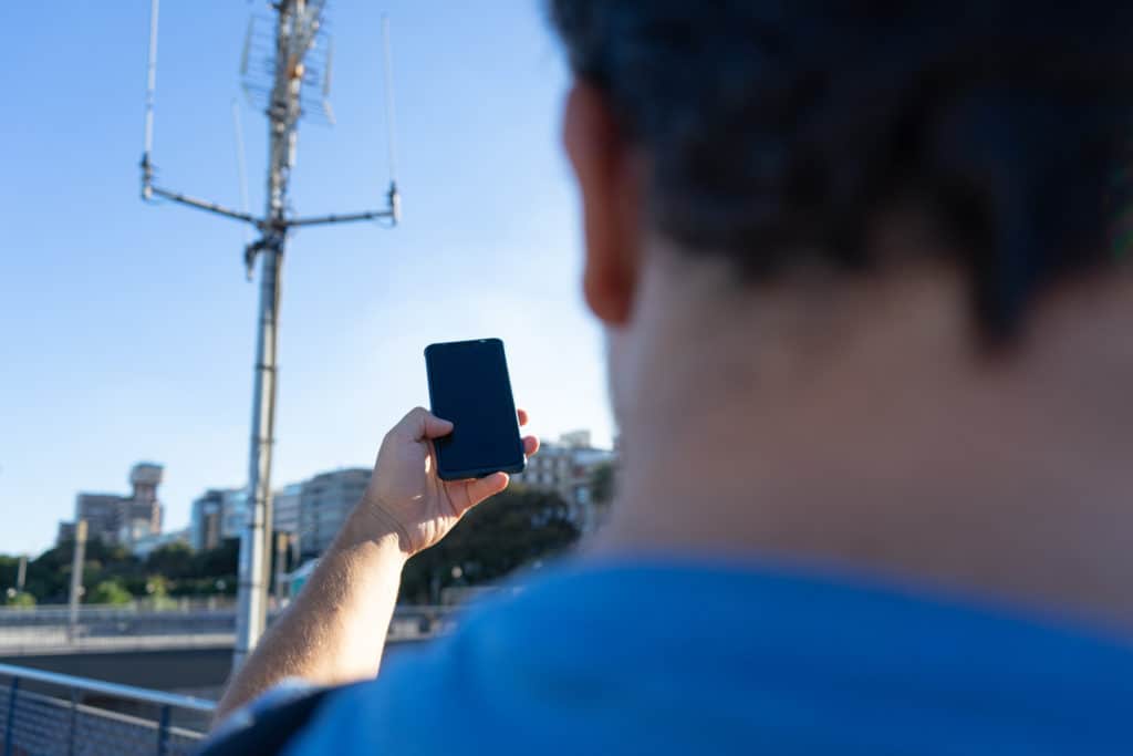Man pointing a smartphone at a cell tower wondering if is mobile data is on or off
