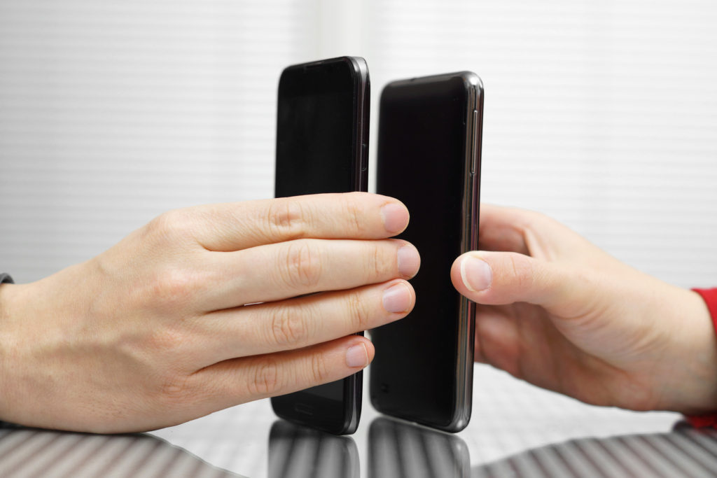 Two hands each holding smartphones sending files over NFC instead of Bluetooth