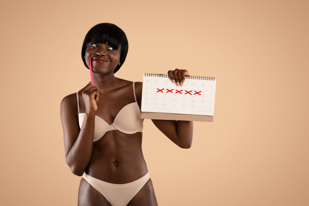 Woman in underwear holding pen and calendar to track her period.