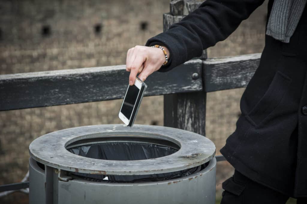 Person dropping burner smartphone into trash to protect his phone number