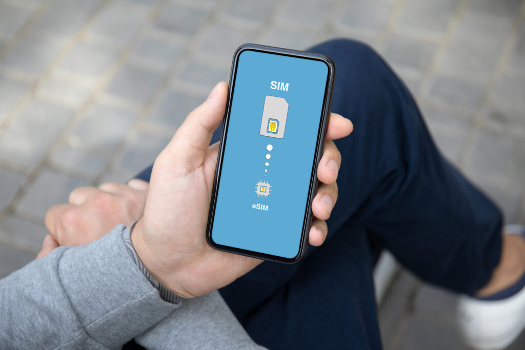 Person sitting cross-legged holding a smartphone with SIM to eSIM graphic on the screen considering how often should a SIM card be replaced