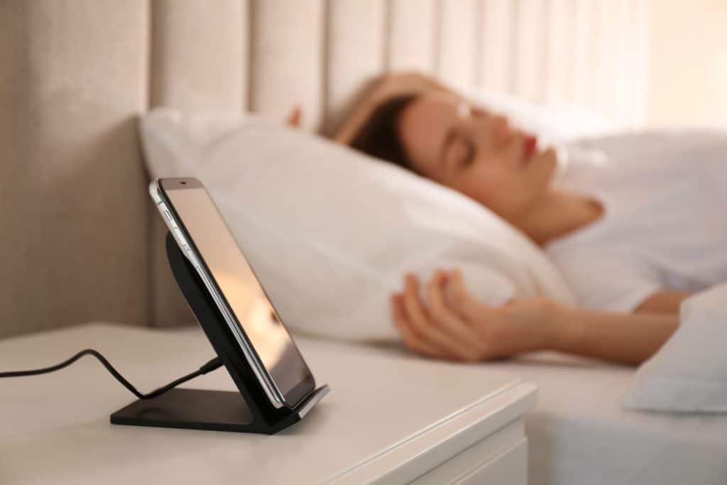 Smartphone on charging stand near bed while woman sleeps. Is it bad charge all night?