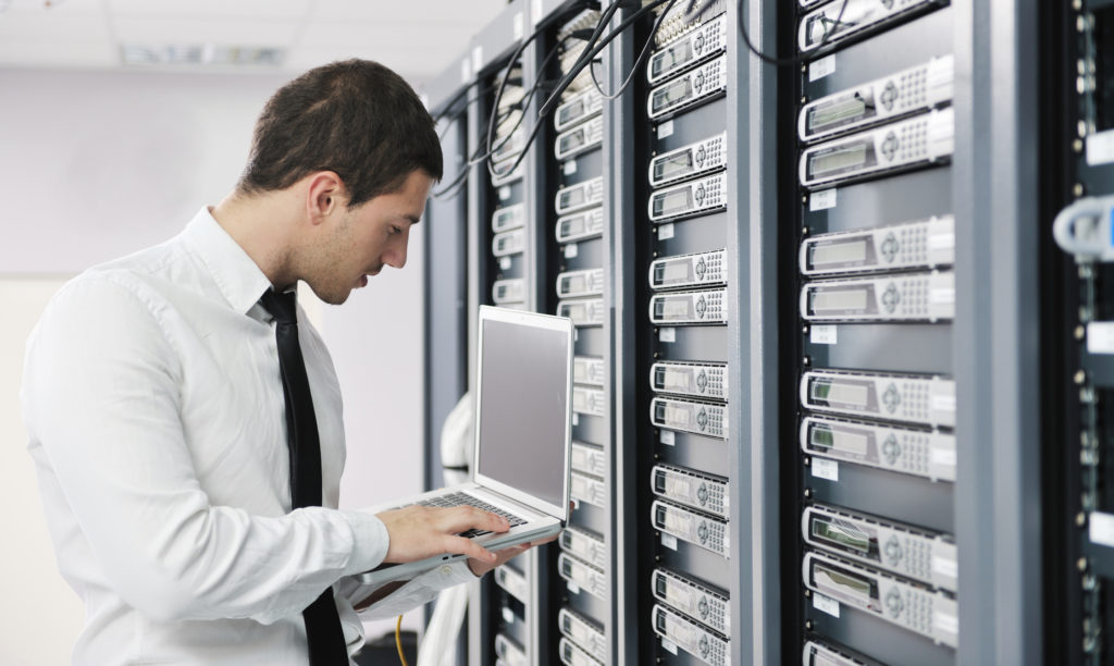 IT professional holding laptop next to servers while inspecting weakness in cyber security