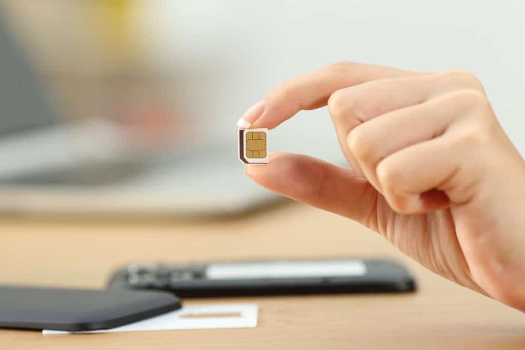 Focus on woman's hand holding a removed SIM chip with a burner phone in the background