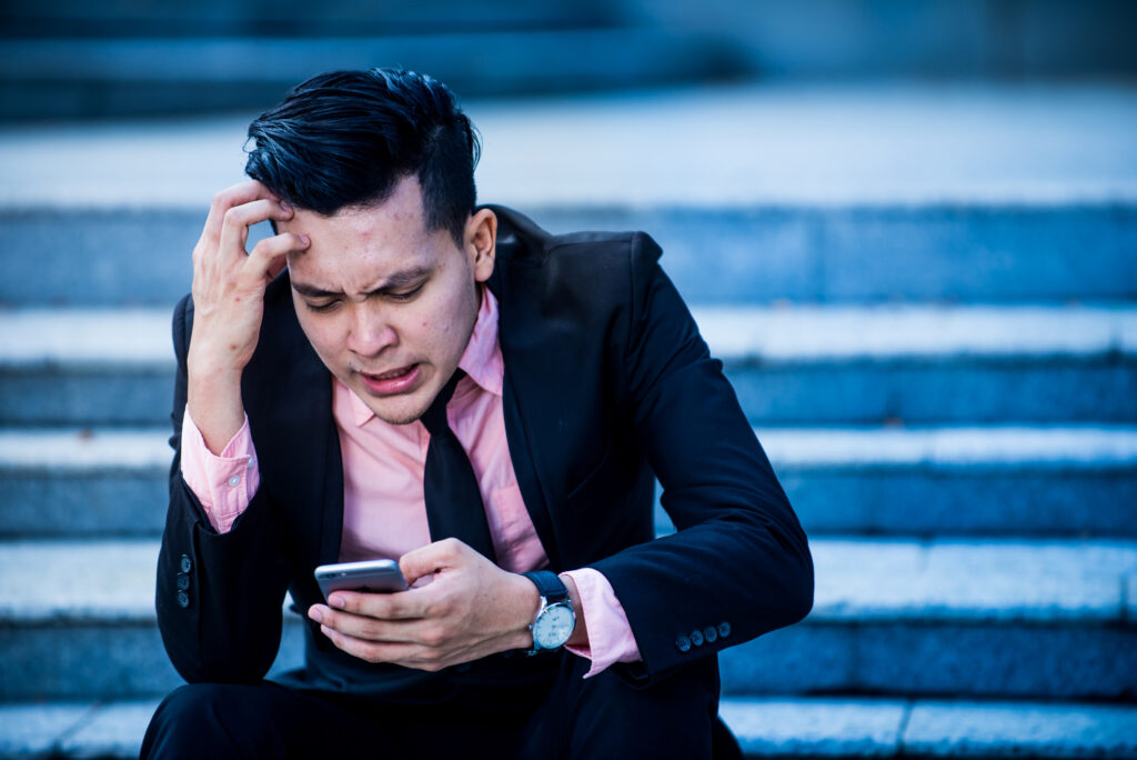 Stressed businessman holding smartphone worried his phone won't ring when it's dead