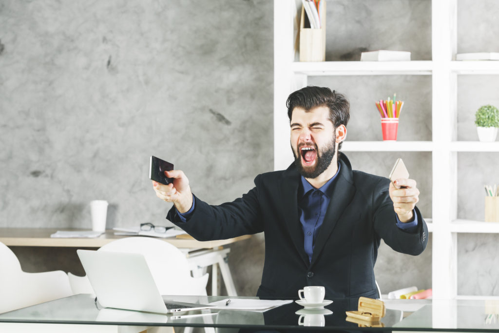 Businessman at his desk holding both his personal and work phone while yelling
