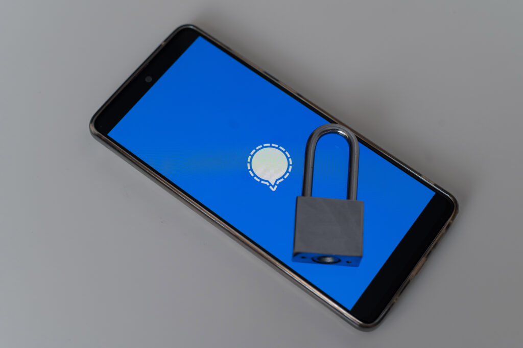 Smartphone with a padlock sitting on top while displaying the Signal Messenger start up screen